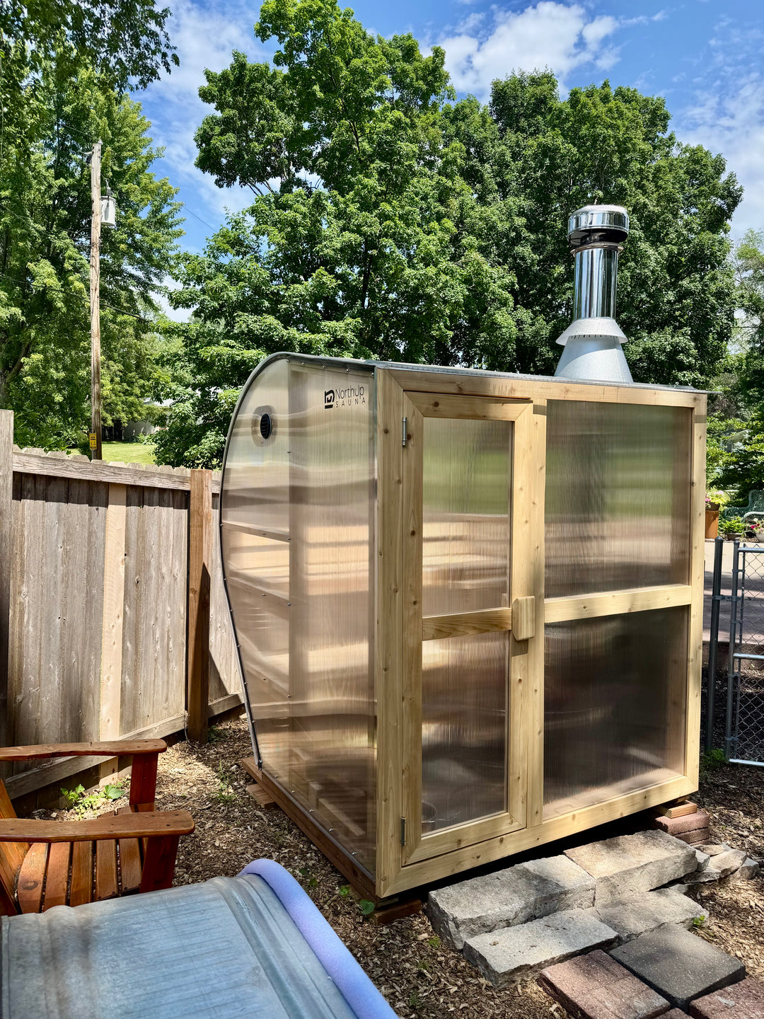NorthUp Curve sauna installed in a backyard next to a fence.