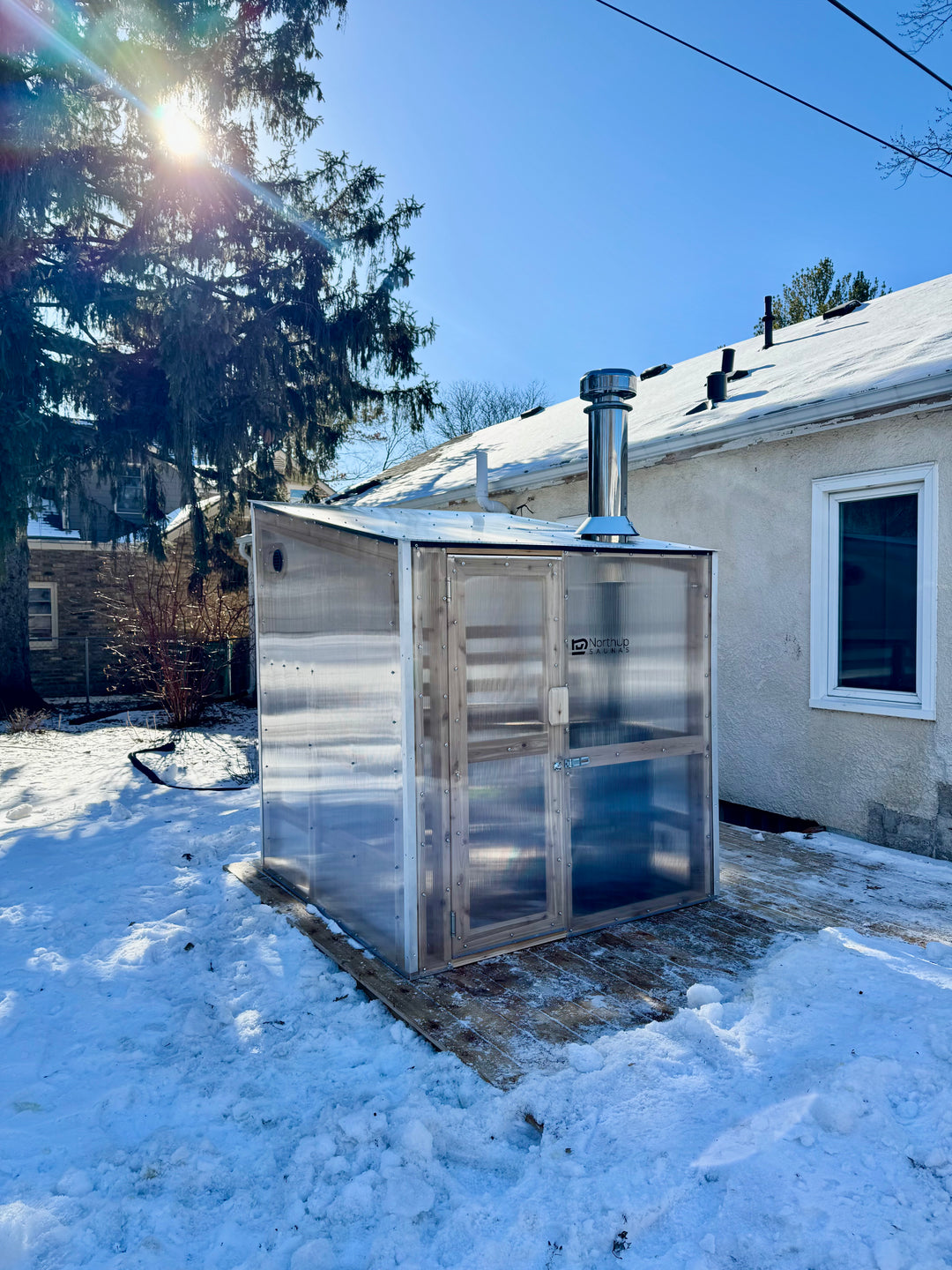 Sunlight passing through trees and NorthUp Core sauna on a snowy landscape