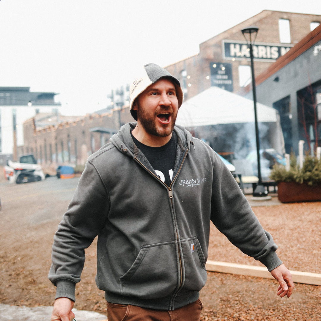 Owner of NorthUp saunas in a gray hoodie and brown pants holding a green bucket outdoors with buildings in the background.