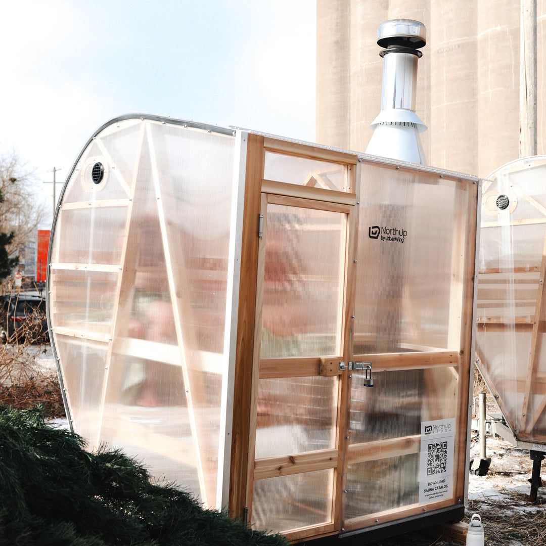 NorthUp Curve exterior sauna view of transparent panels and wood-fired chimney.
