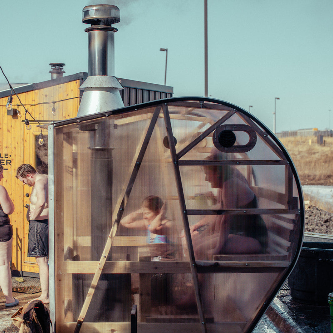 NorthUp Curve side view from outside. People visible and enjoying the sauna through transparent sauna walls.