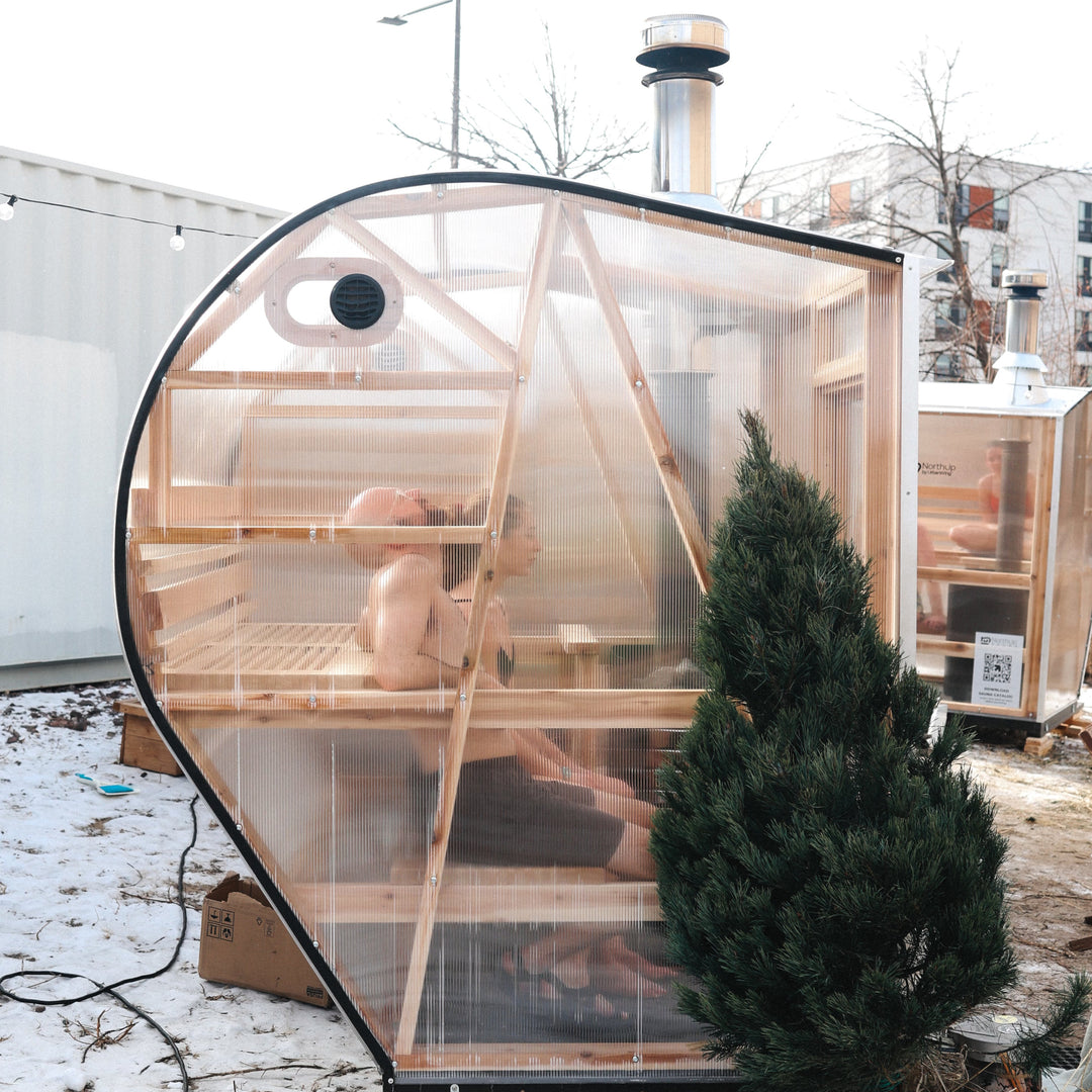 Exterior side view of two people on sauna benches inside of a NorthUp curve sauna. 